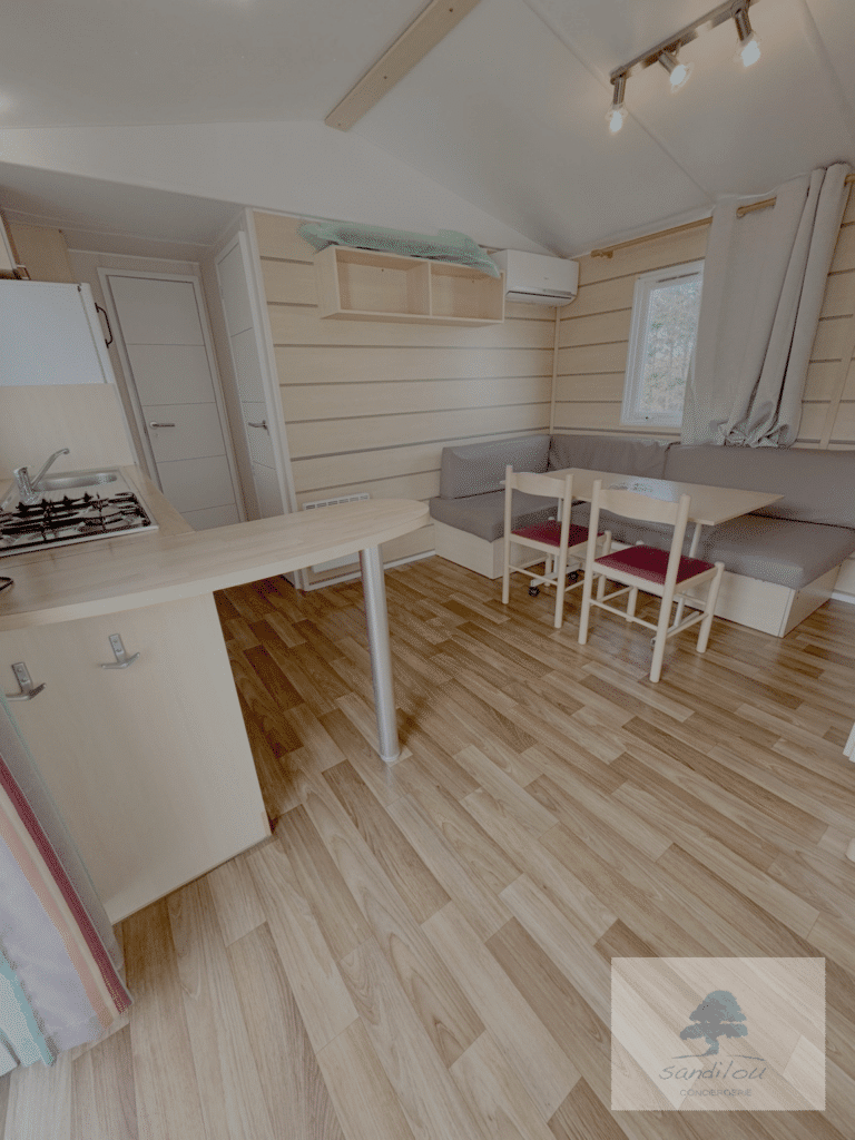 Intérieur d'un mobil-home Sandilou Conciergerie avec cuisine équipée, coin repas et salon chaleureux tout en bois.